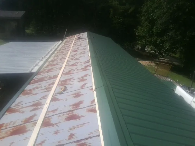Old rusted panels beside newly installed green metal roofing — Wind Damage Roof Repair by Roofing Brothers in Smithsburg