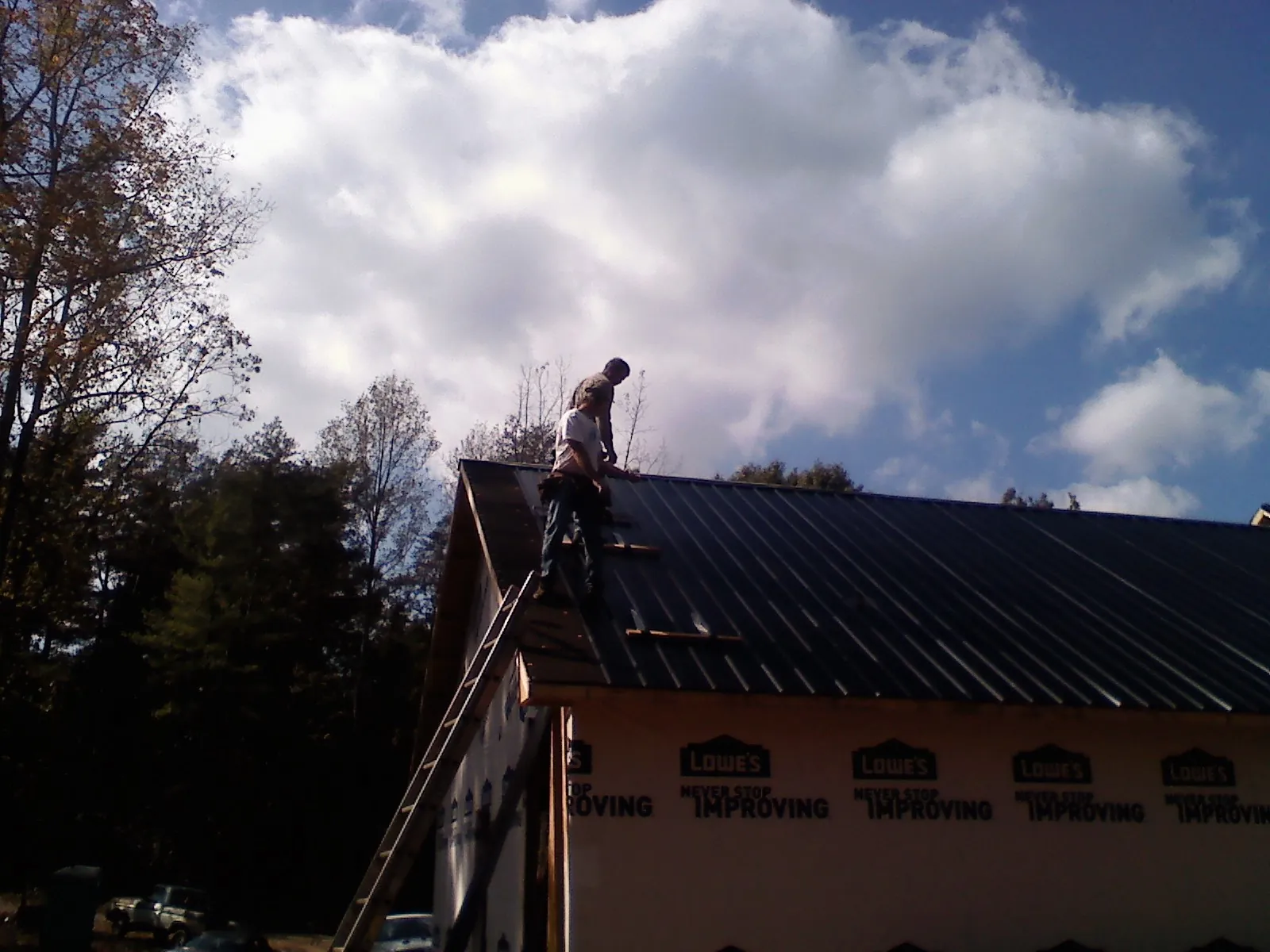 Roofer fastening dark metal panels high against a cloudy sky, from a Roof Inspection job in Smithsburg